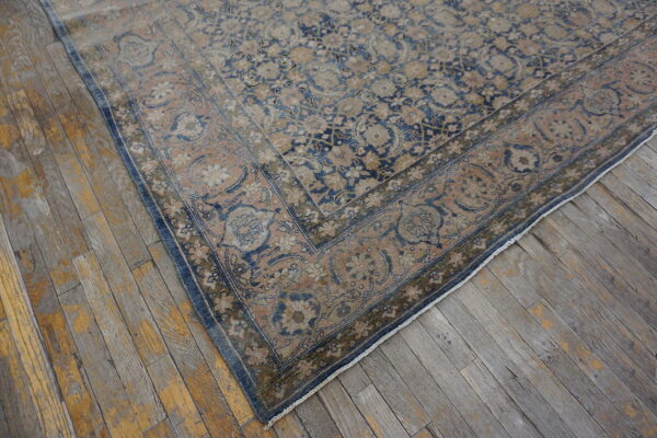 Faded blue and blush patterned rug corner with an ornate border on rustic plank flooring.