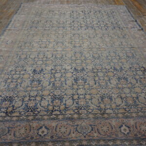 Ornate patterned rug in faded blue, tan, and rose tones resting on a rustic wood floor.