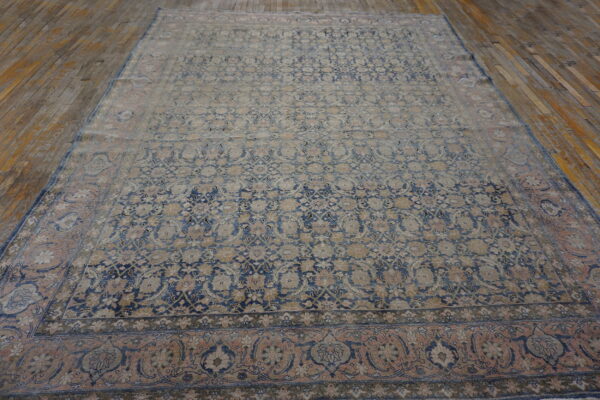 Ornate patterned rug in faded blue, tan, and rose tones resting on a rustic wood floor.