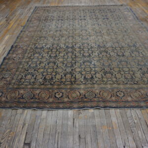 Large navy and beige patterned area rug with an elaborate border resting on worn wood plank flooring.