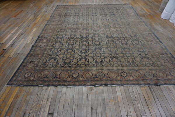 Large navy and beige patterned area rug with an elaborate border resting on worn wood plank flooring.