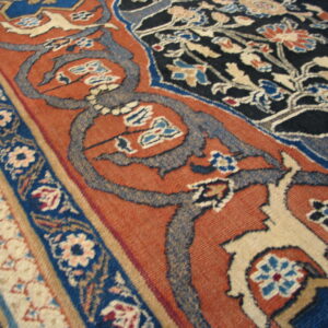 Traditional rug pattern in rust and navy with detailed floral motifs and cream-colored accents.