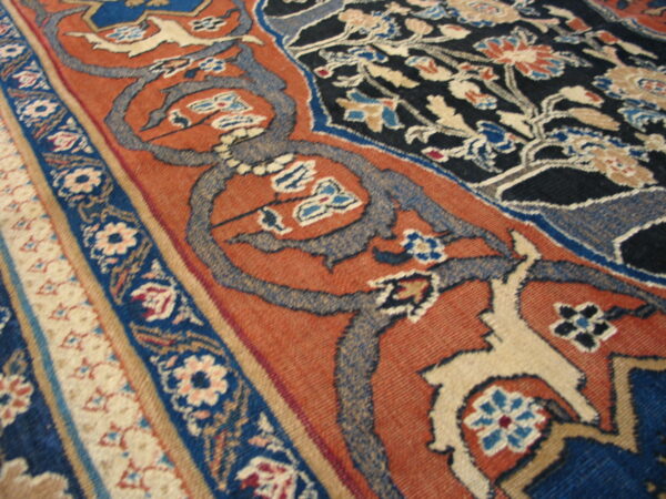 Traditional rug pattern in rust and navy with detailed floral motifs and cream-colored accents.