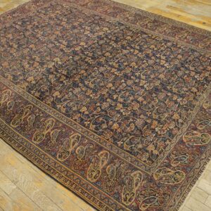 Navy and gold floral rug with maroon paisley border covering a light, distressed wood floor.