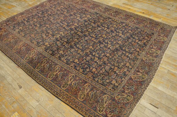 Navy and gold floral rug with maroon paisley border covering a light, distressed wood floor.