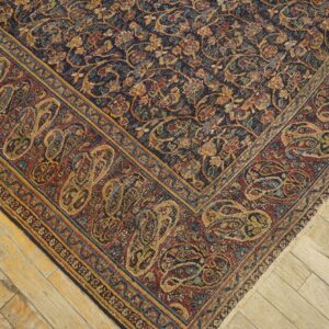 Corner view of a dark navy and red traditional rug with intricate paisley borders on worn wooden floorboards.