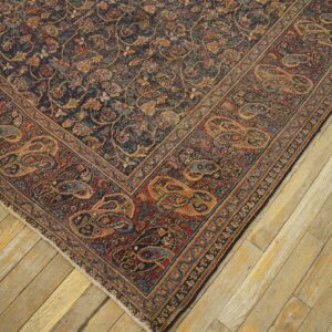 Dark traditional rug corner showing dense floral field and wide rust paisley border on light wood planks.