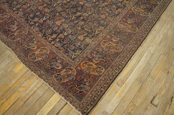 Dark traditional rug corner showing dense floral field and wide rust paisley border on light wood planks.