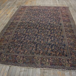 Dark blue rug with dense multicolored floral motifs and a wide burgundy paisley border on distressed wood planks.