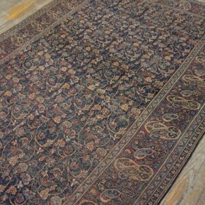 A dark blue rug with intricate floral motifs and a rust border featuring large paisley designs sits on wooden floors.