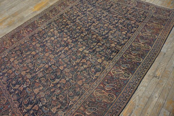 A dark blue rug with intricate floral motifs and a rust border featuring large paisley designs sits on wooden floors.