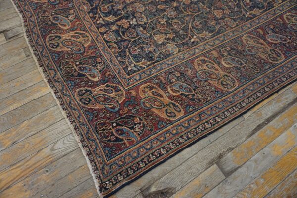 Intricate red and navy traditional rug with paisley borders rests on distressed wood flooring with yellow paint.
