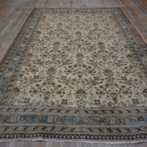 Traditional cream and brown floral rug with a light blue border lying on distressed wood flooring.