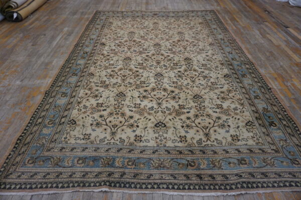 Traditional cream and brown floral rug with a light blue border lying on distressed wood flooring.