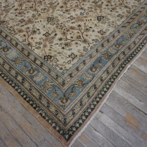 Traditional beige and brown floral rug featuring a prominent dusty blue border on distressed gray plank flooring.