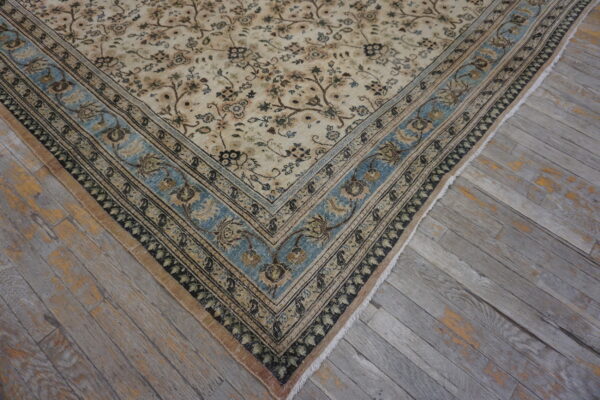 Traditional beige and brown floral rug featuring a prominent dusty blue border on distressed gray plank flooring.