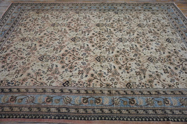Cream rug with dense scrolling floral pattern and contrasting light blue and dark brown borders.