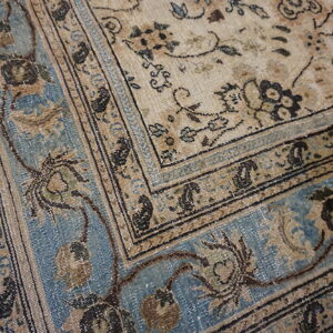 Low-pile rug detail with faded beige, distressed blue, and dark brown traditional floral patterns and borders.