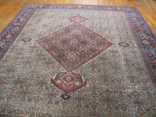 Large traditional beige and red rug with a central diamond medallion and floral design on wood floor.