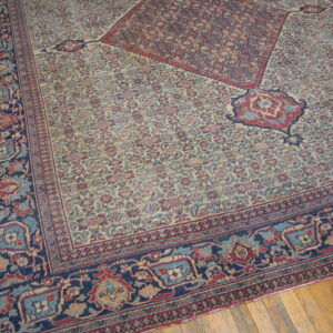 Intricate low-pile rug featuring red, blue, and cream floral designs, a navy border, and corner motifs on wood flooring.