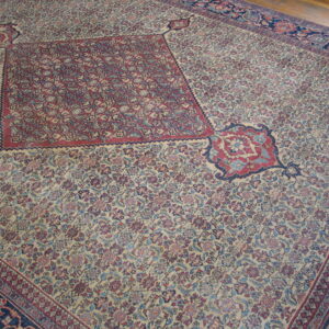 Densely patterned traditional rug featuring a large red medallion on a cream field with blue and red motifs.
