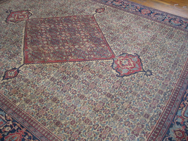 Densely patterned traditional rug featuring a large red medallion on a cream field with blue and red motifs.
