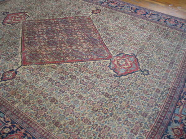 Intricate floral rug with a cream field, red medallion, blue motifs, and a dark border, laid on wood floor.