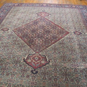 A large traditional rug with a detailed ivory field, a burgundy diamond medallion, and a dark blue border on wood floors.