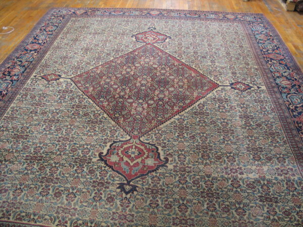 A large traditional rug with a detailed ivory field, a burgundy diamond medallion, and a dark blue border on wood floors.