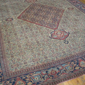 Large, traditional cream-colored rug with dense floral pattern, red medallion, navy border, lying on wood floor.
