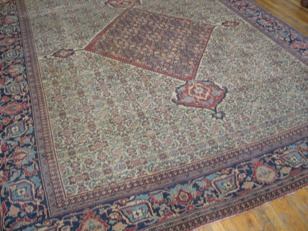 Large, traditional cream-colored rug with dense floral pattern, red medallion, navy border, lying on wood floor.