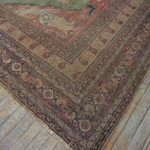 Faded red and sage green traditional rug corner lies on distressed, gray and yellow painted wooden planks.