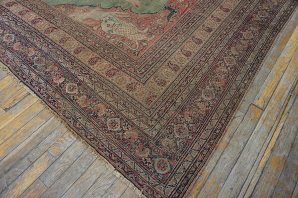 Faded red and sage green traditional rug corner lies on distressed, gray and yellow painted wooden planks.