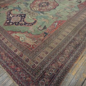 A faded green and coral antique-style rug with animal motifs rests on distressed wood floors.