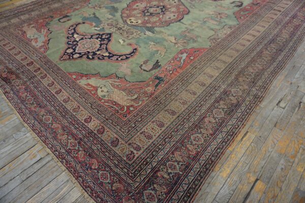 A faded green and coral antique-style rug with animal motifs rests on distressed wood floors.