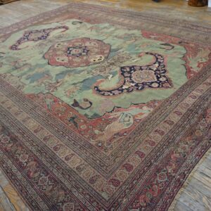 Ornate light green and rust patterned rug with figures and a medallion on light wood plank flooring.