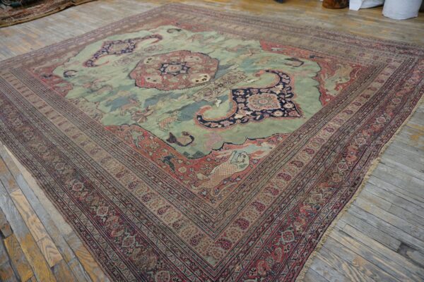 Ornate light green and rust patterned rug with figures and a medallion on light wood plank flooring.