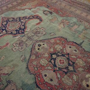 Distressed, low-pile rug with a blue-green field and traditional red and navy animal motifs on wood planks.