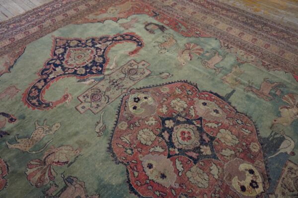 Distressed, low-pile rug with a blue-green field and traditional red and navy animal motifs on wood planks.