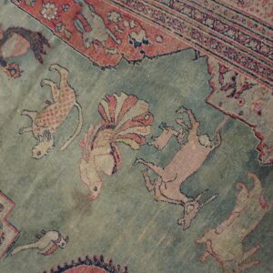 A close-up view of a low-pile rug features a muted sage field with stylized animal figures.