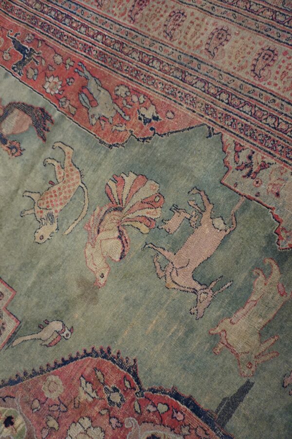 A close-up view of a low-pile rug features a muted sage field with stylized animal figures.