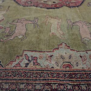 Low-pile rug detail showing muted pink figures on a sage green field framed by detailed multicolored geometric borders.