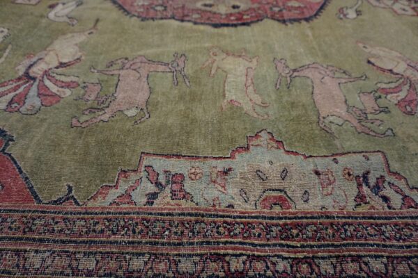 Low-pile rug detail showing muted pink figures on a sage green field framed by detailed multicolored geometric borders.