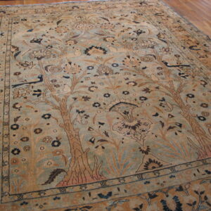 Tan and blue-green rug displaying detailed floral and animal motifs on hardwood floor.