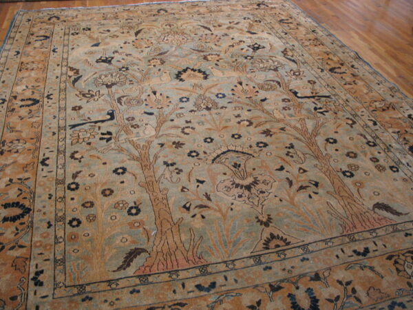 Tan and blue-green rug displaying detailed floral and animal motifs on hardwood floor.