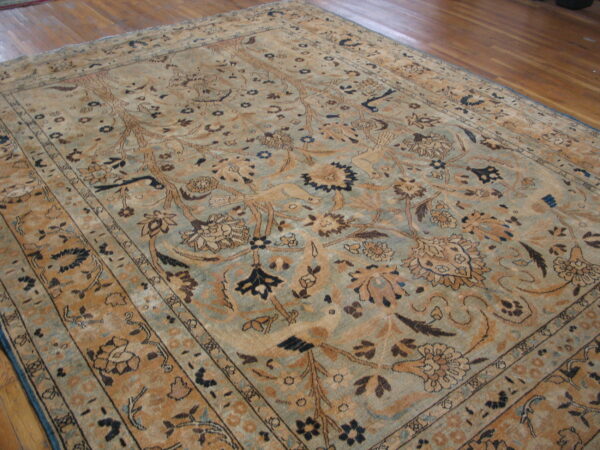 Low-pile rug with a complex botanical pattern in faded blue-green, tan, and brown on hardwood.