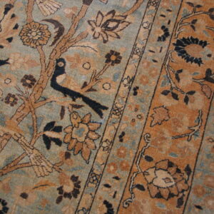 Close-up of a rug featuring an intricate tree-of-life and border pattern in muted blue, rust, and brown colors.