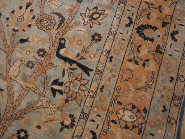 Close-up of a rug featuring an intricate tree-of-life and border pattern in muted blue, rust, and brown colors.