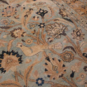 Muted teal and tan low-pile rug detail showing elaborate floral designs and stylized birds.