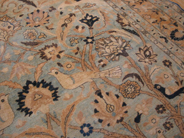 Muted teal and tan low-pile rug detail showing elaborate floral designs and stylized birds.